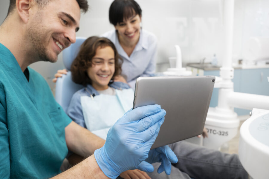 Imagem mostrando um dentista usando tecnologia digital em consulta odontológica com paciente jovem e assistente, demonstrando odontologia digital em ação.