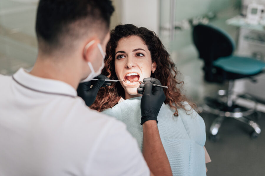 atleta sentada na cadeira em um consultório de dentista com a boca aberta, enquanto o dentista do esporte faz um tratamento em seu dente.