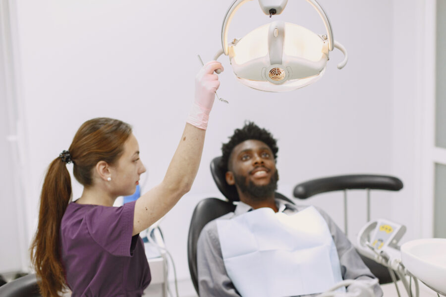 Imagem de uma dentista cuidando do paciente, que está deitado na maca para o procedimento ser realizado.