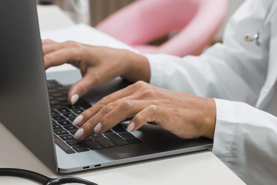 Mãos de um profissional de saúde digitando em um laptop, utilizando um aplicativo receita saúde em um consultório.