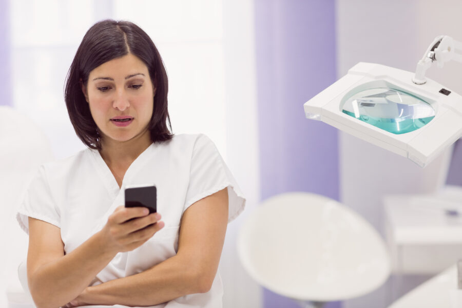 Uma mulher em uniforme branco olhando para um celular, refletindo sobre sua receita de saúde em um ambiente clínico.
