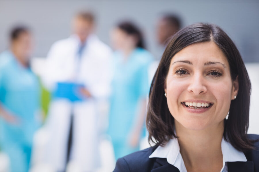 Mulher sorridente em foco com profissionais de saúde ao fundo, simbolizando o CIOSP 2025, um evento importante na área da odontologia.